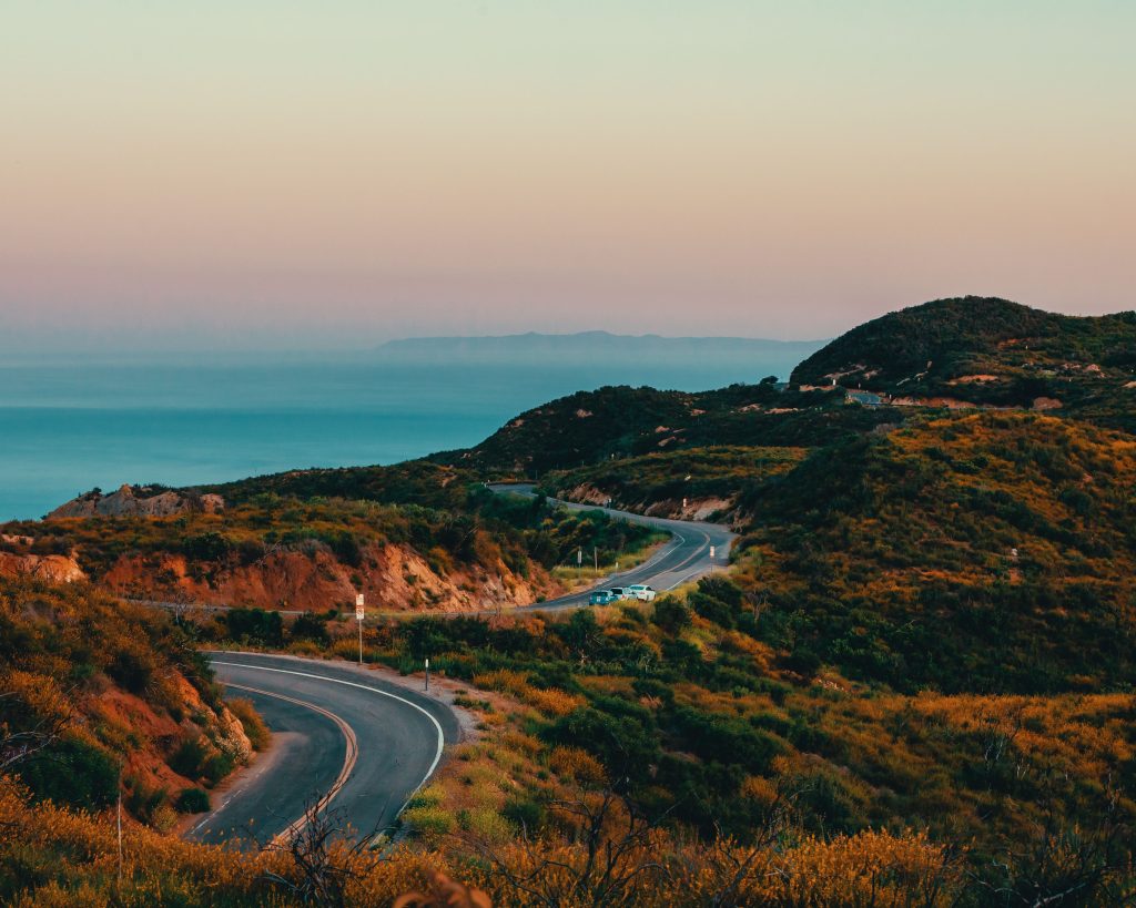 A winding canyon road above Malibu at sunset, coastline visible in the distance